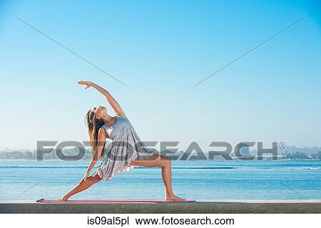 Stock Image - Young woman practicing yoga on pier at Pacific beach, San Diego, California, USA. Fotosearch