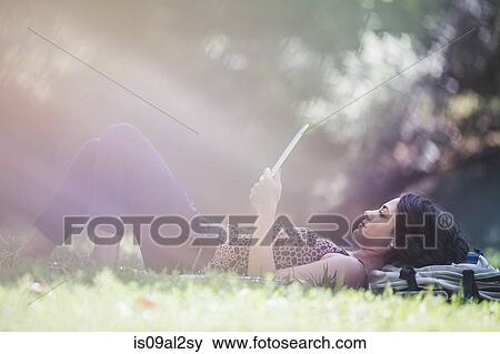 Stock Photo - Young woman relaxing in city park reading digital tablet. Fotosearch