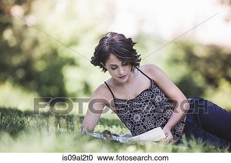 Stock Image - Young woman sitting in city park studying textbook. Fotosearch