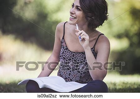 Stock Photo - Young woman sitting in city park studying textbook. Fotosearch