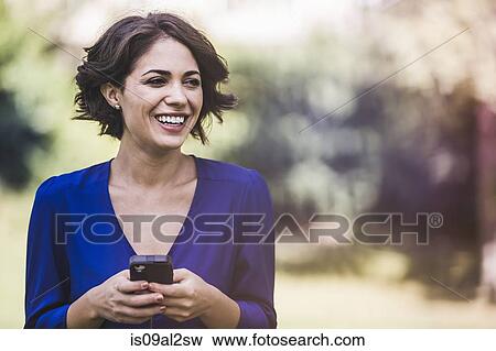 Stock Photo - Young woman texting on smartphone in city park laughing. Fotosearch