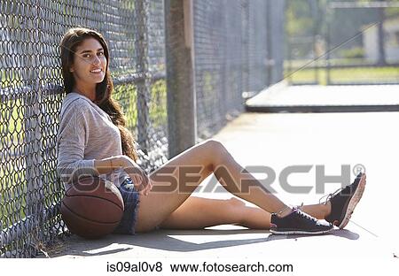 Stock Photo - Young woman with basketball sitting by wire fence. Fotosearch