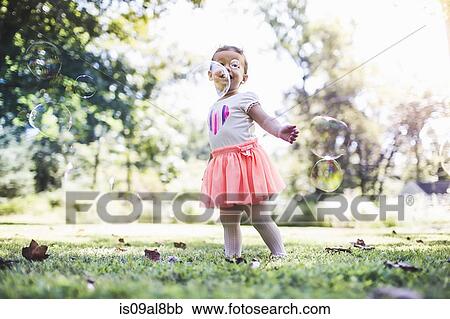 Stock Image - Baby girl playing with bubbles in garden. Fotosearch