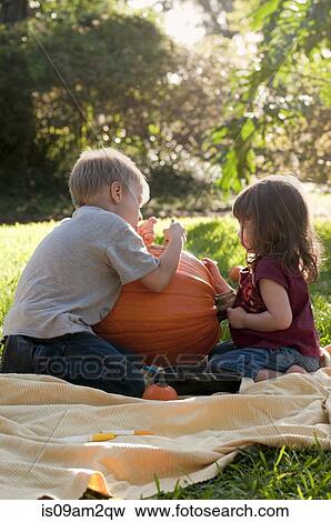 Stock Photo - Brother and sister drawing on pumpkin. Fotosearch