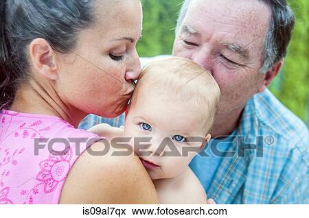 Stock Photo - Close up of mother and grandfather kissing baby girl. Fotosearch