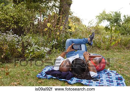 Couple lying on grass watching movie on tablet View Large Photo Image Stock Image - Couple lying on grass watching movie on tablet. Fotosearch