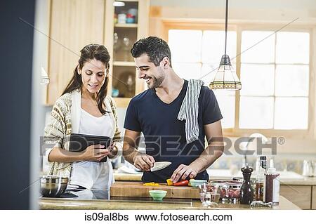 Stock Photograph - Couple preparing food and using digital tablet in kitchen. Fotosearch