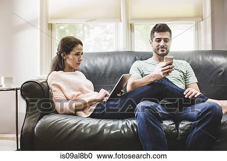 Stock Image - Couple using digital tablet and smartphone on sofa. Fotosearch