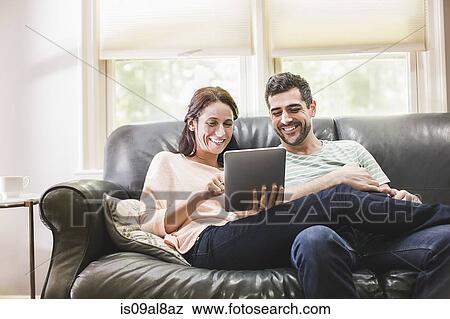 Couple using digital tablet on sofa View Large Photo Image Stock Photo - Couple using digital tablet on sofa. Fotosearch