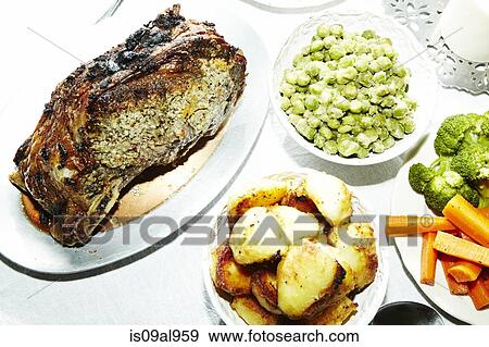 Stock Photo - Dinner meal of roast meat with potatoes, carrots, broccoli and broad beans on table. Fotosearch