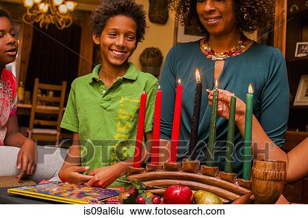 Stock Photograph - Family lighting kinara candles, celebrating Kwanzaa. Fotosearch