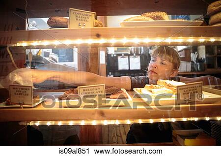 Female shop assistant picking up cake from display cabinet in country store View Large Photo Image Stock Image - Female shop assistant picking up cake from display cabinet in country store. Fotosearch