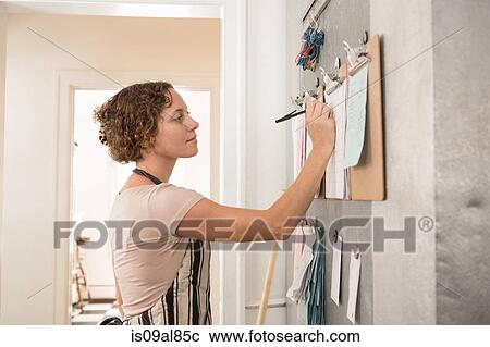 Stock Image - Female shop assistant writing on wall clipboards in kitchen at country store. Fotosearch
