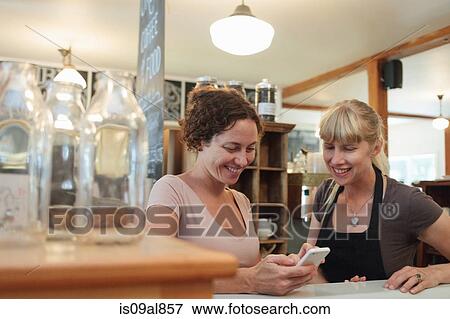 Female shop assistants looking at smartphone in country store View Large Photo Image Stock Photo - Female shop assistants looking at smartphone in country store. Fotosearch