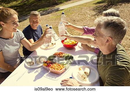Picture - Four mature adult friends raising a toast with water bottles in park. Fotosearch