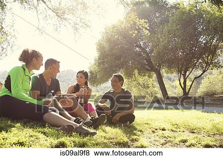 Stock Photo - Four mature male and female runners sitting chatting in park. Fotosearch