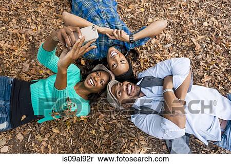 Stock Photography - Friends taking selfie lying on fallen autumn leaves. Fotosearch