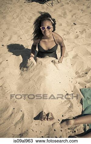 Stock Image - Girl buried in sand on beach, Truro, Massachusetts, Cape Cod, USA. Fotosearch