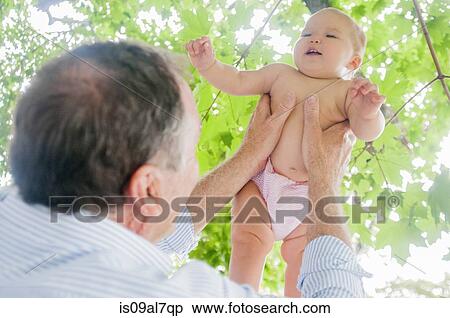 Stock Photography - Grandfather holding up baby granddaughter in park. Fotosearch
