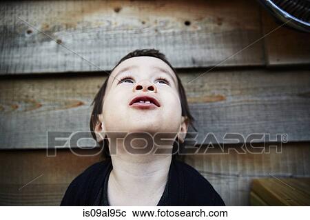 Stock Image - Low angle portrait of male toddler in front of shed looking up. Fotosearch
