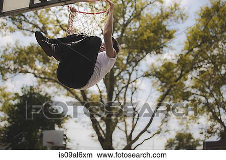 Picture - Low angle view of young male basketball hanging from basketball hoop. Fotosearch