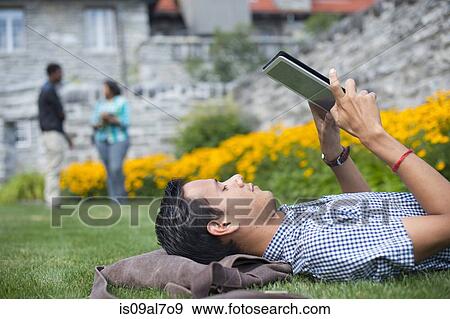Male student lying on grass using digital tablet View Large Photo Image Stock Photo - Male student lying on grass using digital tablet. Fotosearch