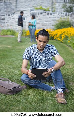 Male student sitting on grass using digital tablet View Large Photo Image Stock Photo - Male student sitting on grass using digital tablet. Fotosearch
