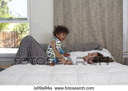 Stock Image - Male toddler sitting on top of mother on bed. Fotosearch