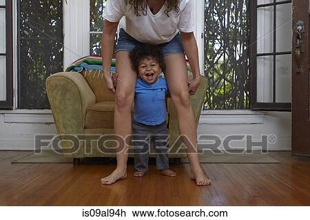 Stock Image - Male toddler taking first steps with mother in sitting room. Fotosearch