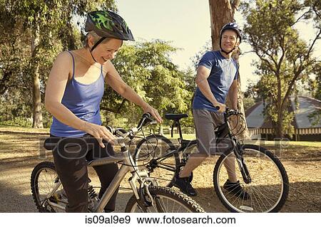 Stock Photo - Mature couple chatting on bicycles in park. Fotosearch
