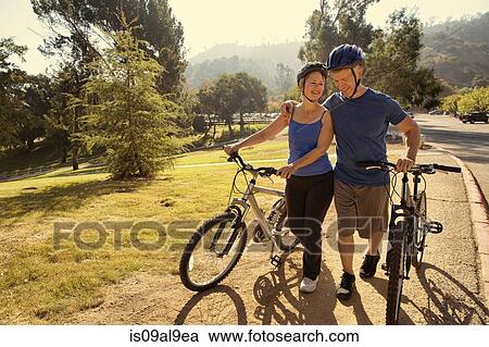 Mature couple chatting whilst pushing bicycles in park View Large Photo Image Stock Image - Mature couple chatting whilst pushing bicycles in park. Fotosearch