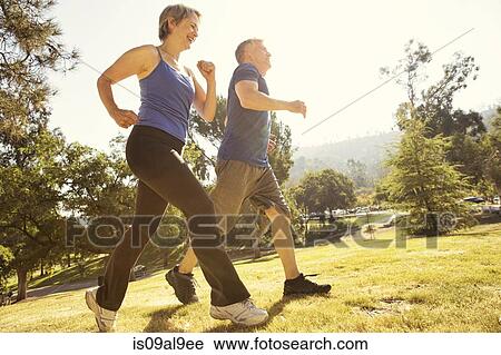 Mature couple power walking in park View Large Photo Image Stock Image - Mature couple power walking in park. Fotosearch