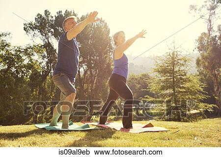 Stock Image - Mature couple practicing yoga position in park. Fotosearch
