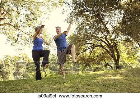 Stock Image - Mature couple practicing yoga positions in park. Fotosearch