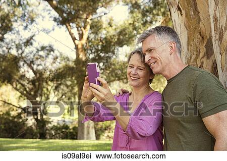 Mature couple using touchscreen on smartphone in park View Large Photo Image Stock Image - Mature couple using touchscreen on smartphone in park. Fotosearch
