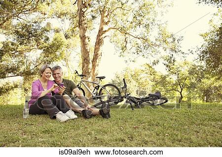 Mature cycling couple sitting in park looking at smartphone View Large Photo Image Stock Image - Mature cycling couple sitting in park looking at smartphone. Fotosearch