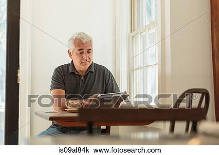 Stock Image - Mature man using digital tablet in country store cafe. Fotosearch