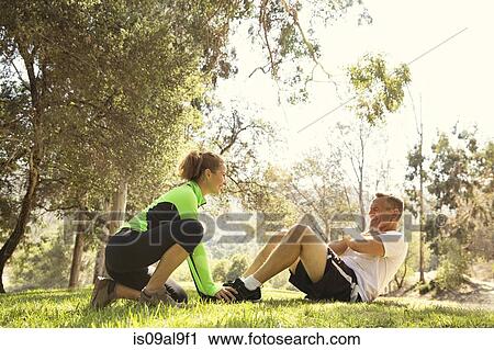 Stock Image - Mature running couple doing sit ups in park. Fotosearch