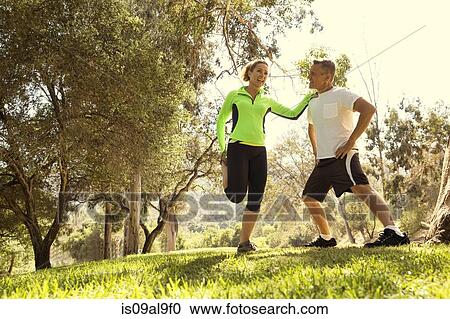 Stock Image - Mature running couple warming up in park. Fotosearch