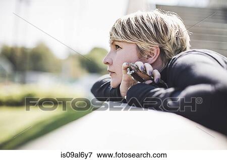 Mature woman gazing from footbridge wall holding onto smartphone View Large Photo Image Stock Photo - Mature woman gazing from footbridge wall holding onto smartphone. Fotosearch