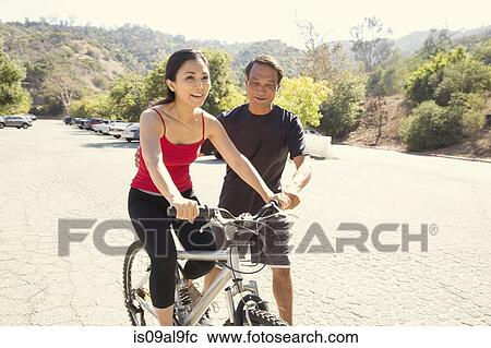 Stock Image - Mature woman learning to ride bicycle in park. Fotosearch