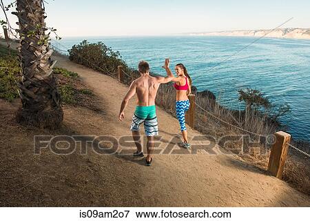 Stock Photo - Mid adult man and young giving high five on path by sea. Fotosearch