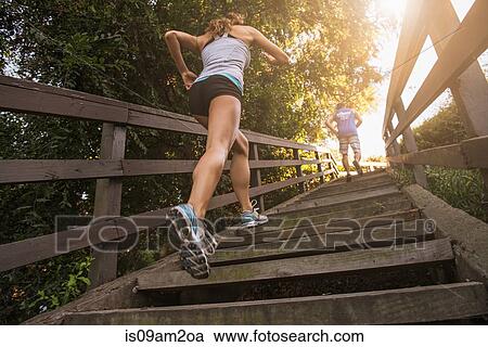 Stock Image - Mid adult man and young woman running up steps, rear, low angle view. Fotosearch