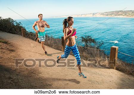 Mid adult man and young woman running on path by sea View Large Photo Image Stock Photograph - Mid adult man and young woman running on path by sea. Fotosearch