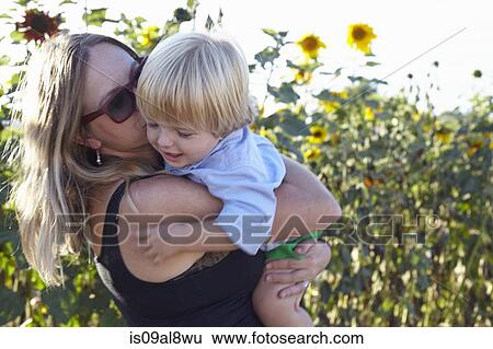 Stock Photograph - Mid adult woman and toddler hugging in sunflower field. Fotosearch