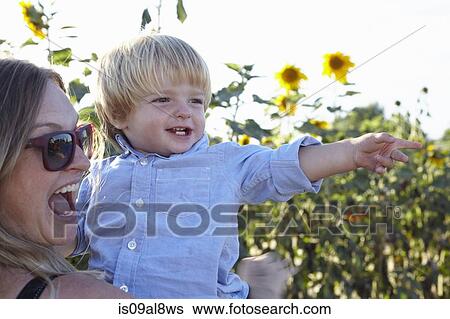 Stock Photograph - Mid adult woman and toddler son pointing in sunflower field. Fotosearch