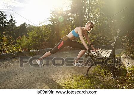 Mid adult woman runner stretching against park bench View Large Photo Image Stock Photography - Mid adult woman runner stretching against park bench. Fotosearch