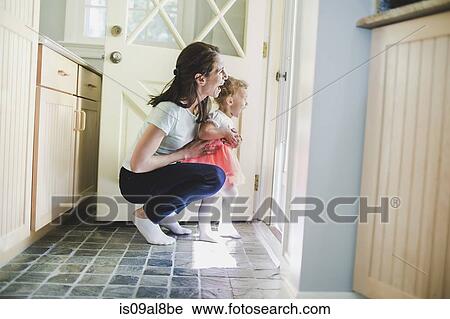Stock Image - Mother and daughter laughing at doorway. Fotosearch