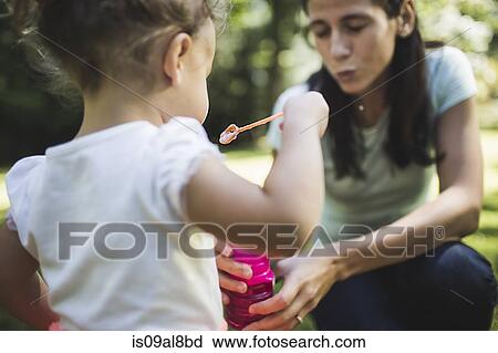 Stock Image - Mother and daughter playing bubbles in garden. Fotosearch