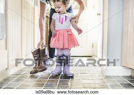 Stock Photograph - Mother and daughter putting on boots in kitchen. Fotosearch